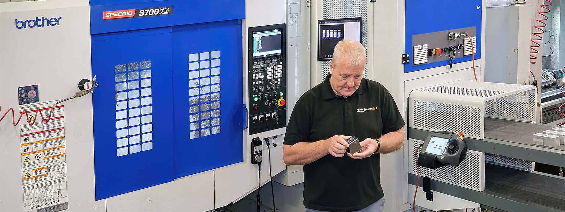 Operator inspecting a machined component beside a Brother Speedio CNC machine at WMT, showcasing precision engineering and automated machining technology.